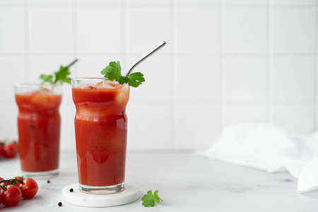 two glasses of tomato juice with a sprig of parsley on a white table, close-upの写真素材