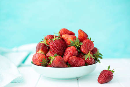 large ripe sweet strawberries in a ceramic plate on a turquoise background, close-upの写真素材