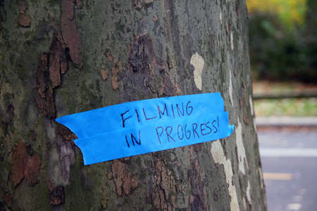 Filming in progress sign on a tree at the park with a blue tapeの写真素材