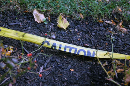 The yellow Caution tape laying on the ground with the soil and the grass with spare leavesの写真素材