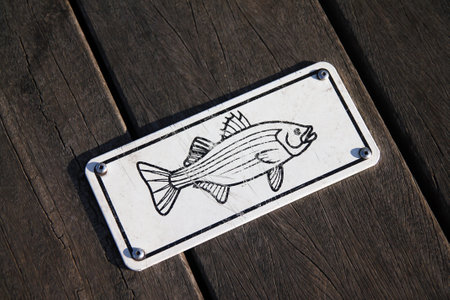 A black and white fish characteristic sign on a wooden board on a pier on the sea
