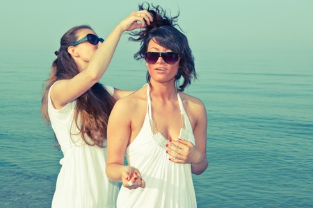 Young Woman Dress Her Friend's Hairs at Seasideの写真素材