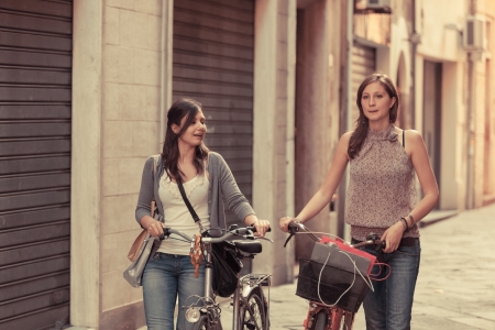 Two Beautiful Women Walking in the City with Bicycles and Bagsの写真素材