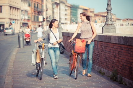 Two Beautiful Women Walking in the City with Bicycles and Bagsの写真素材