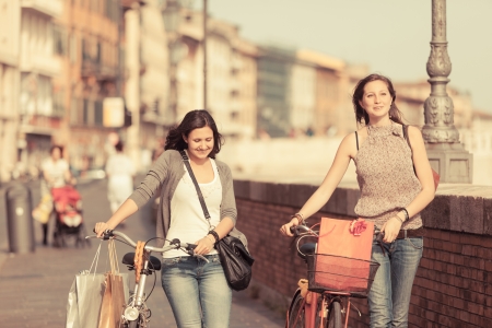 Two Beautiful Women Walking in the City with Bicycles and Bagsの写真素材