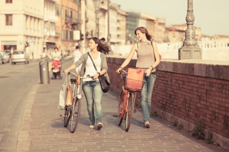 Two Beautiful Women Walking in the City with Bicycles and Bagsの写真素材