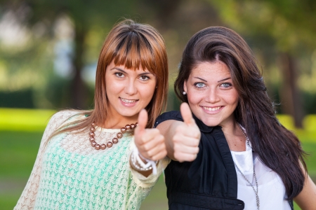 Happy Female Friends at Park with Thumbs Upの写真素材