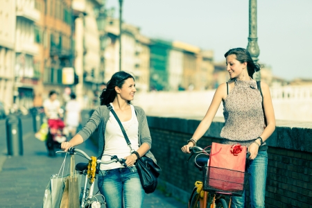 Two Beautiful Women Walking in the City with Bicycles and Bagsの写真素材
