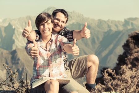 Young Couple with Thumbs Up at Top of Mountainの写真素材