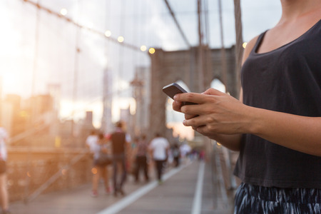 Young Woman Using Smart Phone on Brooklyn Bridgeの写真素材