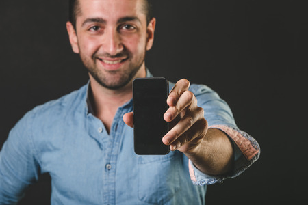 Young Man Showing Smart Phone Display, Black Backgroundの写真素材
