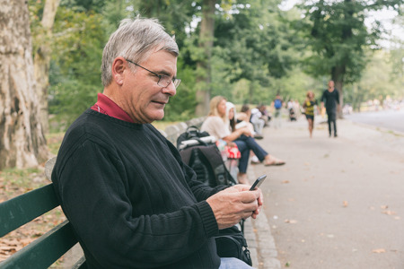 Retired Senior Man at Park, Typing on Mobile, Smiling Expressionの写真素材