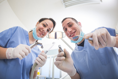 Cheerful Dentists Holding Dental Tools Looking at Camera. Personal or Patient Point of View, POV. They are holding Drill, Mirror, Aspirator and Spreader.の写真素材