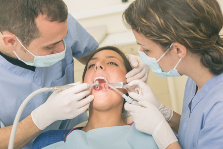 Dentist and Dental Assistant examining Patient teeth. Dentist is a Man, Assistant and Patient are Women. Patient is Relaxed and not scared of Dentist.の写真素材