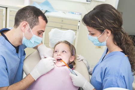 Dentist and Dental Assistant examining Young Girl teeth. Dentist is a Male, Assistant and Patient are Females. Patient is a Young Girl, she's Smiling and not scared of Dentist.の写真素材