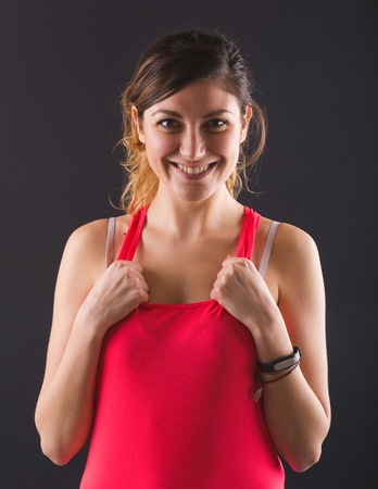 Sporty Young Woman Portrait on Black Background. Shes is Wearing a Red Top and she is Holding Her Hands on the Upper part of the Top.の写真素材