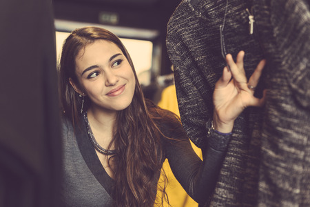 Beautiful girl at clothes shop looking for a dress, rooting around through the shelves. Behind the...