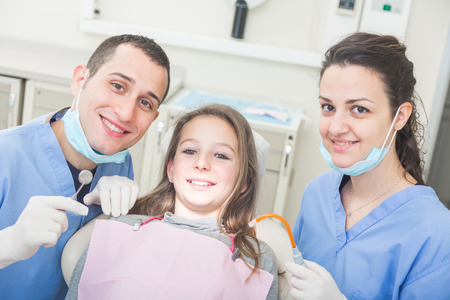 Dentist and dental assistant portrait with young patient. Dentist is a male, assistant and patient are females. All the people are looking at camera with Smiling expressions.の写真素材