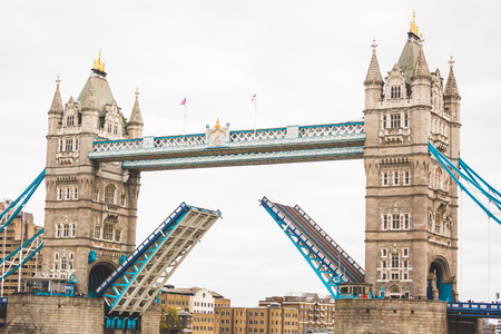 Tower Bridge in London with drawbridge open on a cloudy day with a sail passing through.の写真素材