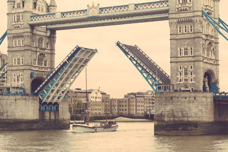 Tower Bridge in London with drawbridge open on a cloudy day with a sail passing through.の写真素材