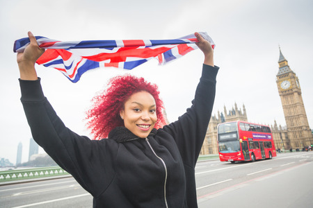 Beautiful redhair woman holding United Kingdom flag, also known as Union Jack, in London with Big Beg and Westminster palace on background.の写真素材