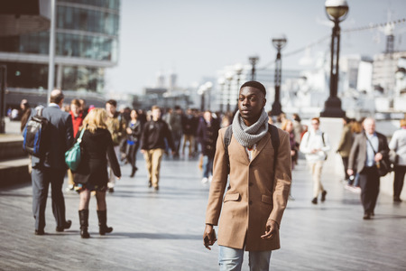 Man walking in London on Thames sidewalk, with blurred people on background. He is looking away. Photo taken on a sunny winter day.