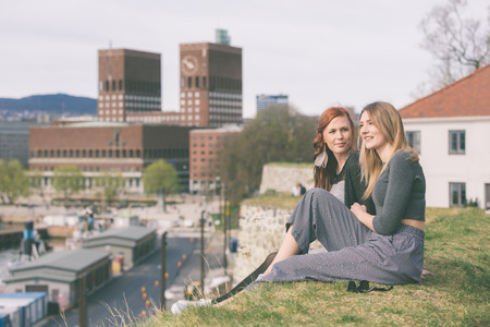 Two beautiful nordic girls enjoying their spare time in Oslo, talking and laughing, with harbour and...