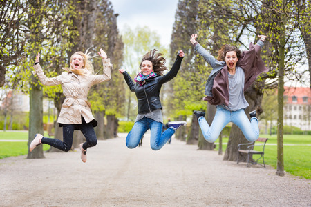 Group of women jumping at park in Copenhagen. They are in their twenties and they are wearing smart casual clothes. Happiness, friendship and success concepts.の写真素材