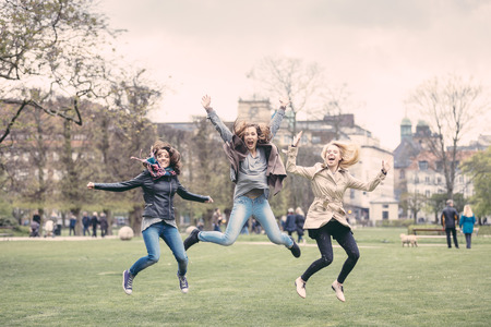 Group of women jumping at park in Copenhagen. They are in their twenties and they are wearing smart casual clothes. Happiness, friendship and success concepts.の写真素材