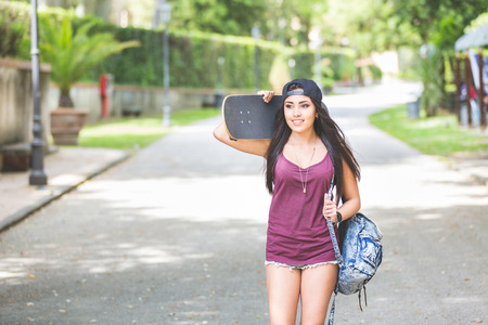 Beautiful girl walking at park holding a skateboard. She is half caucasian and half filipina, she...