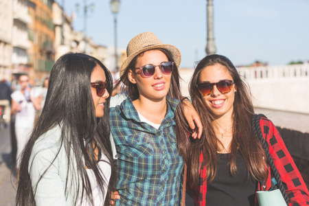 Three happy women walking in the city, talking each other and smiling. This is a mixed race group, one girl is half asian and one is middle eastern. Lifestyle, friendship and urban life concepts.の写真素材