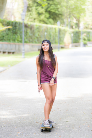Beautiful girl skating at park. She is half caucasian and half filipina, she wears short jeans, a purple tank top and a black cap.の写真素材