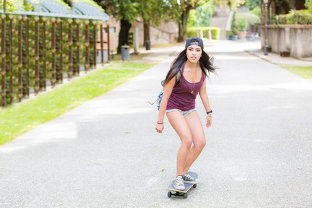Beautiful girl skating at park. She is half caucasian and half filipina, she wears short jeans, a purple tank top and a black cap.の写真素材