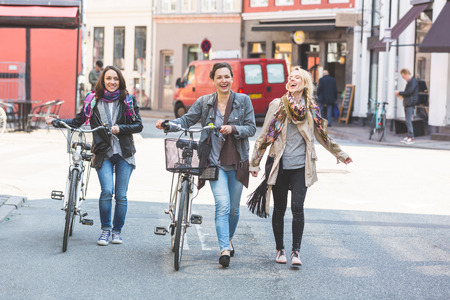 Group of women walking in Copenhagen. They are in their twenties and they are wearing smart casual clothes. Two of them are holding a bicycle, typical mode of transport in Denmark.の写真素材
