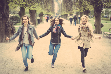 Group of women running at park in Copenhagen. They are in their twenties and they are wearing smart casual clothes. Happiness, friendship and lifestyle concepts.の写真素材