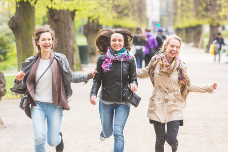 Group of women running at park in Copenhagen. They are in their twenties and they are wearing smart casual clothes. Happiness, friendship and lifestyle concepts.の写真素材
