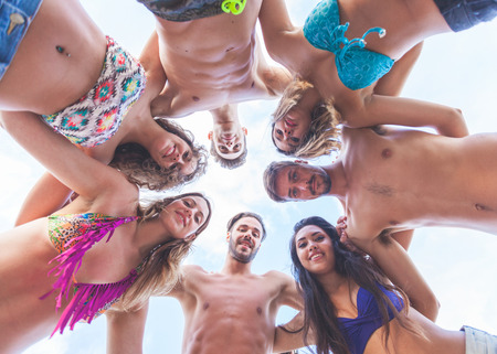 Multiracial group of friends embraced at seaside, bottom view. There are four girls and three boys, all of them are wearing swimsuits.の写真素材