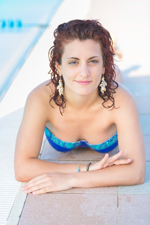Beautiful woman next to swimming pool. She is on her twenties, wearing colourful bikini. Summer and lifestyle concepts.の写真素材