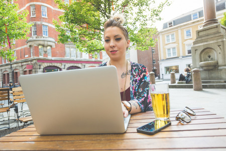 Girl working on her computer outdoor. She is writing on the keyboard while sitting at open air....