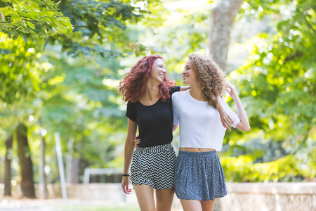 Two girls walking embraced at park. . They are two young girls walking embraced and  smiling to each other. They are having fun together on a summer day.の写真素材