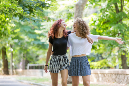 Two girls walking embraced at park. . They are two young girls walking embraced and  smiling to each other. They are having fun together on a summer day.の写真素材