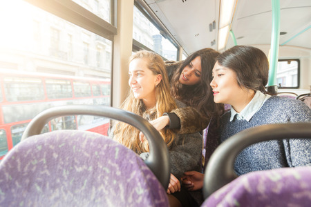 Three women looking out the window from. the bus. They are a mixed group with a caucasian, an asian and a spanish woman. They are friends and they are travelling together by bus.の写真素材