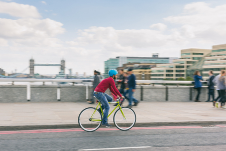 Hipster man cycling on London bridge with Thames river and Tower Bridge on background. He is riding...