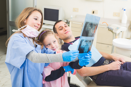 Dentist and dental assistant examining an X-ray image of patient mouth. They are very young girls and the patient is a man. This is a funny  and surreal situation.の写真素材