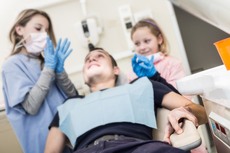 Two little dentist and dental assistant with a threatening look next to their adult patient. Focus on the hand holding at chair. This is a funny  and surreal situation.の写真素材