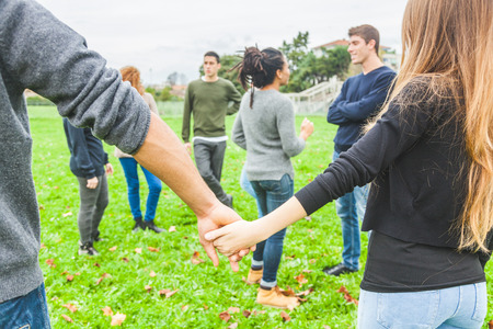 Multiethnic group of friends holding hands in a circle. The focus is on two hands with many other persons on background. Teamwork, integration, community, friendship conceptsの写真素材