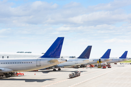 Tails of some airplanes at airport during boarding operations. They are four planes on a sunny day, with a blue sky. Travel and transportation concepts.の写真素材