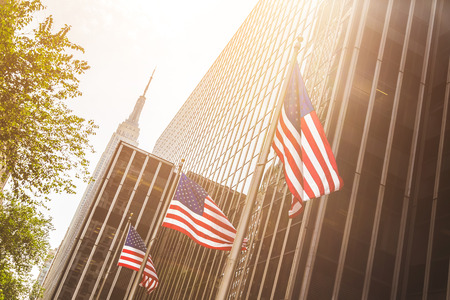 United States flags waving with modern buildings on background in New York. Backlight shot with sun...