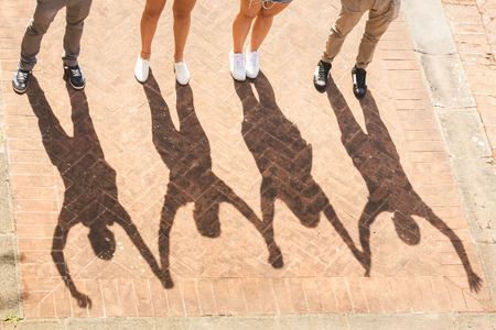 Shadows of friends holding and raising hands  together. They are two girls and two boys, the focus is on their shadows. Togetherness and friendship concepts with an unusal view.の写真素材