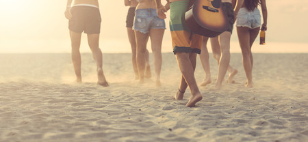Group of friends walking on the beach at sunset. There are four girls and three boys, the sand is blowing, backlight technique, rear view.の写真素材